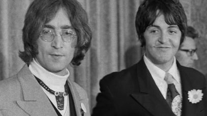 John Lennon looks off to the side, Paul McCartney stands beside him smiling