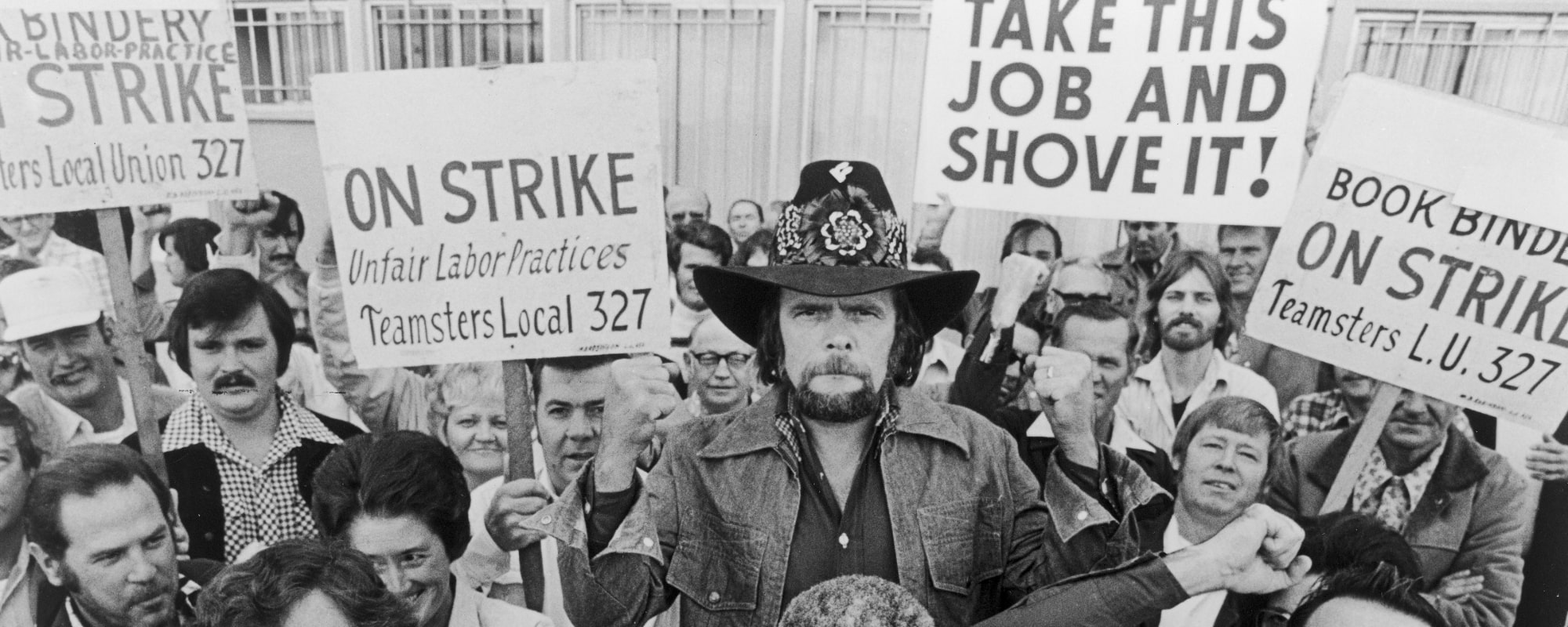 Johnny Paycheck (1938 - 2003) (C) holds a teamsters union sign while joining a group of striking bookbinders, 1977.