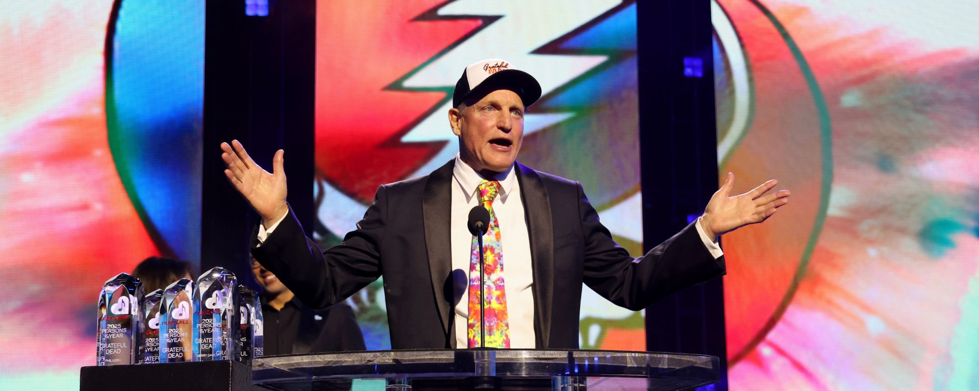 Woody Harrelson standing in front of Grateful Dead logo