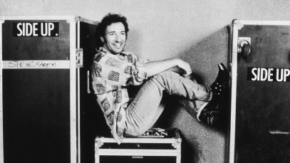 28th July 1992: American musician Bruce Springsteen sits on a trunk with his feet up backstage at the Brendan Byrne Arena in the Meadowlands sports complex, East Rutherford, New Jersey. Springsteen wears a casual shirt with faded jeans and a pair of cowboy boots with chains and metal tips. (Photo by Keith Meyers/New York Times Co./Getty Images)